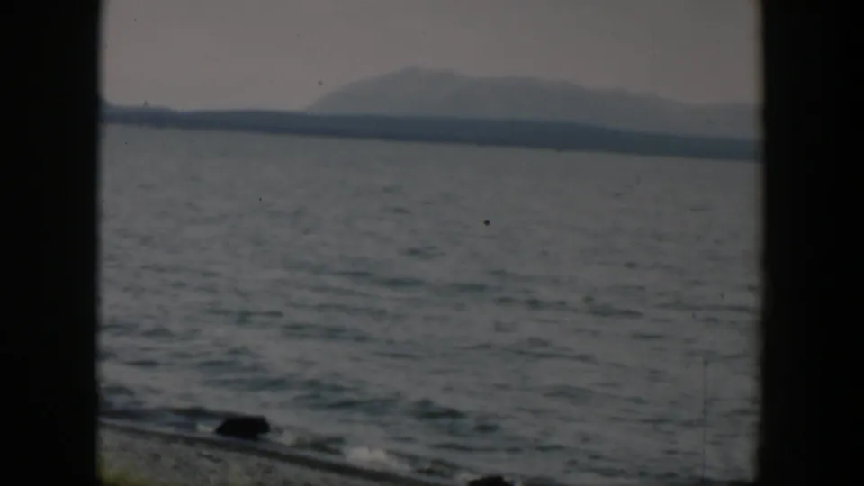 1951 8mm Wyoming frame showing open water, a distant mountain shoreline, and dark window framing near the lower edge.
