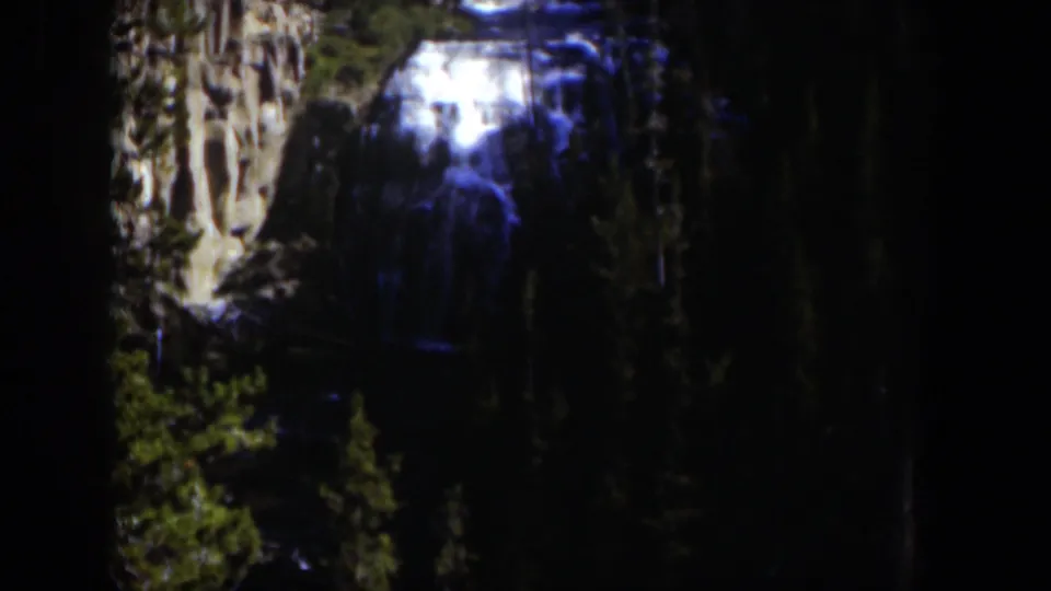 1951 Wyoming 8mm view of a waterfall seen through shadowed trees and pale rock walls.