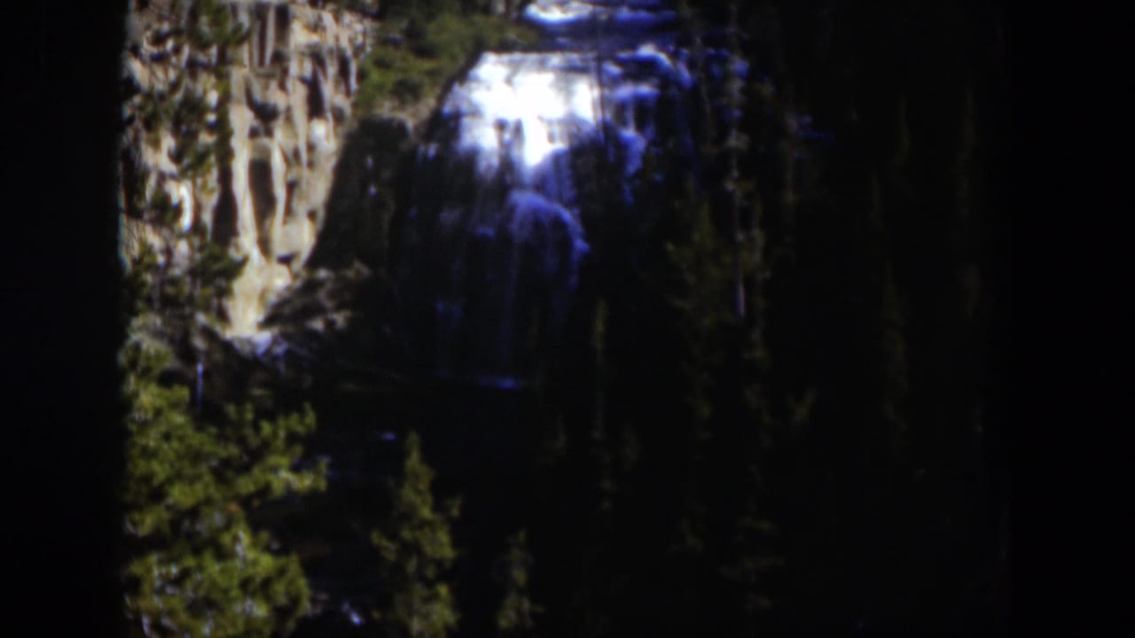 Final 1951 Wyoming 8mm frame centers the waterfall, with evergreens and cliff faces around the falling water.