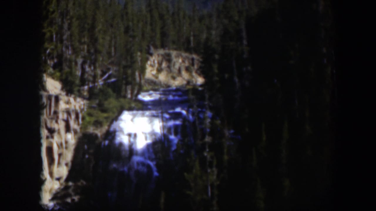 1951 Wyoming 8mm frame of a bright waterfall framed by dense trees and rough canyon walls.
