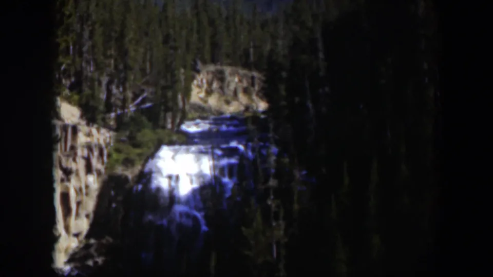 1951 Wyoming 8mm frame of a bright waterfall framed by dense trees and rough canyon walls.