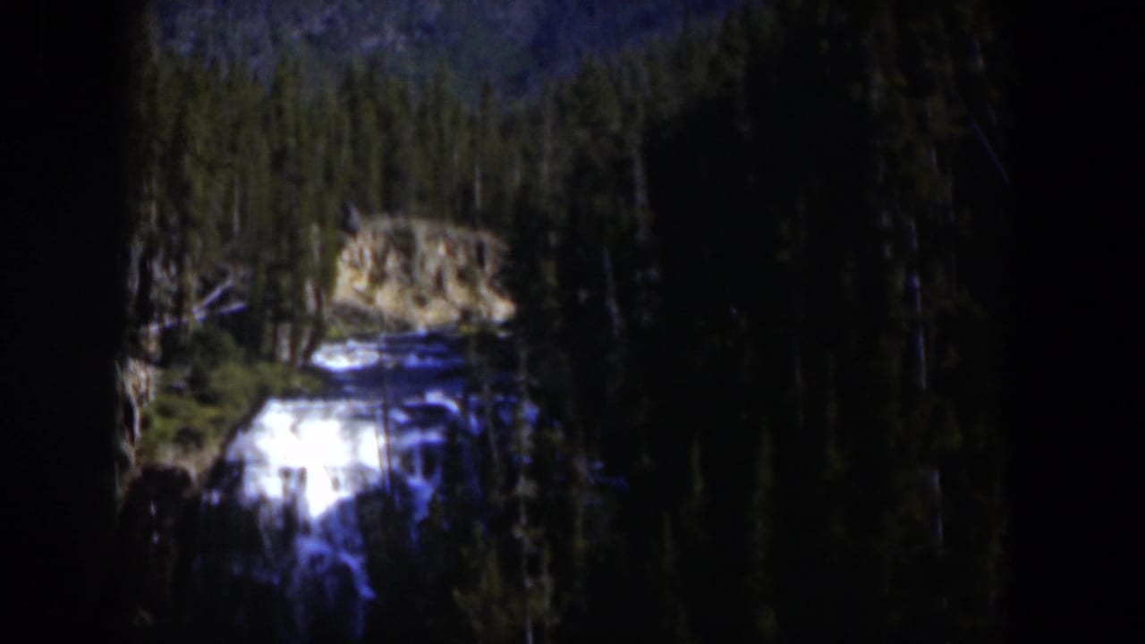 1951 Wyoming home-movie frame with white water, rock faces, and evergreen trees in a mountain setting.