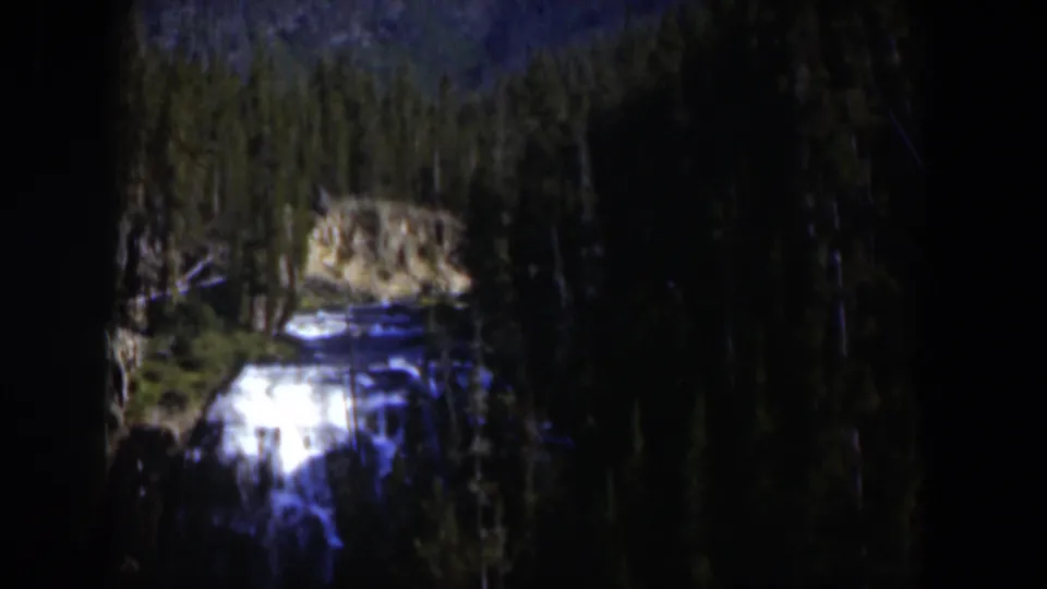 1951 Wyoming home-movie frame with white water, rock faces, and evergreen trees in a mountain setting.
