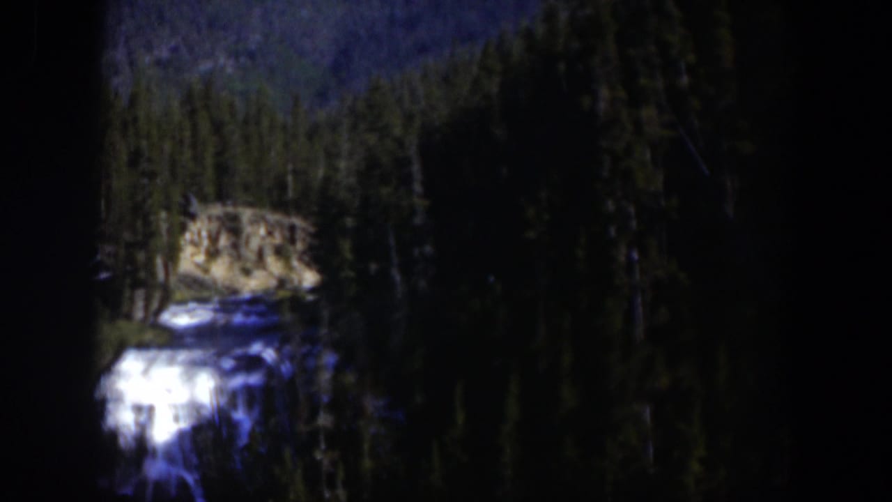 Vintage 8mm frame from Wyoming showing a waterfall and stream partly obscured by dark exposure and forest shadows.