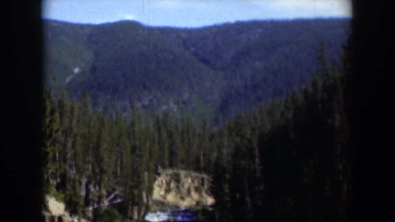 Wyoming 1951 8mm frame showing layered wooded ridges, evergreen trees, and a rocky feature partly obscured by window framing.
