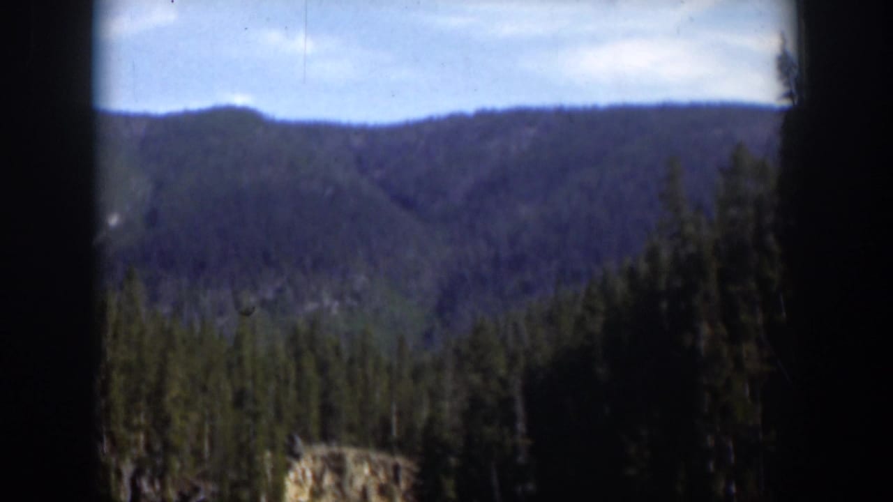 Forested mountain ridge under blue sky, seen through dark 8mm frame borders.