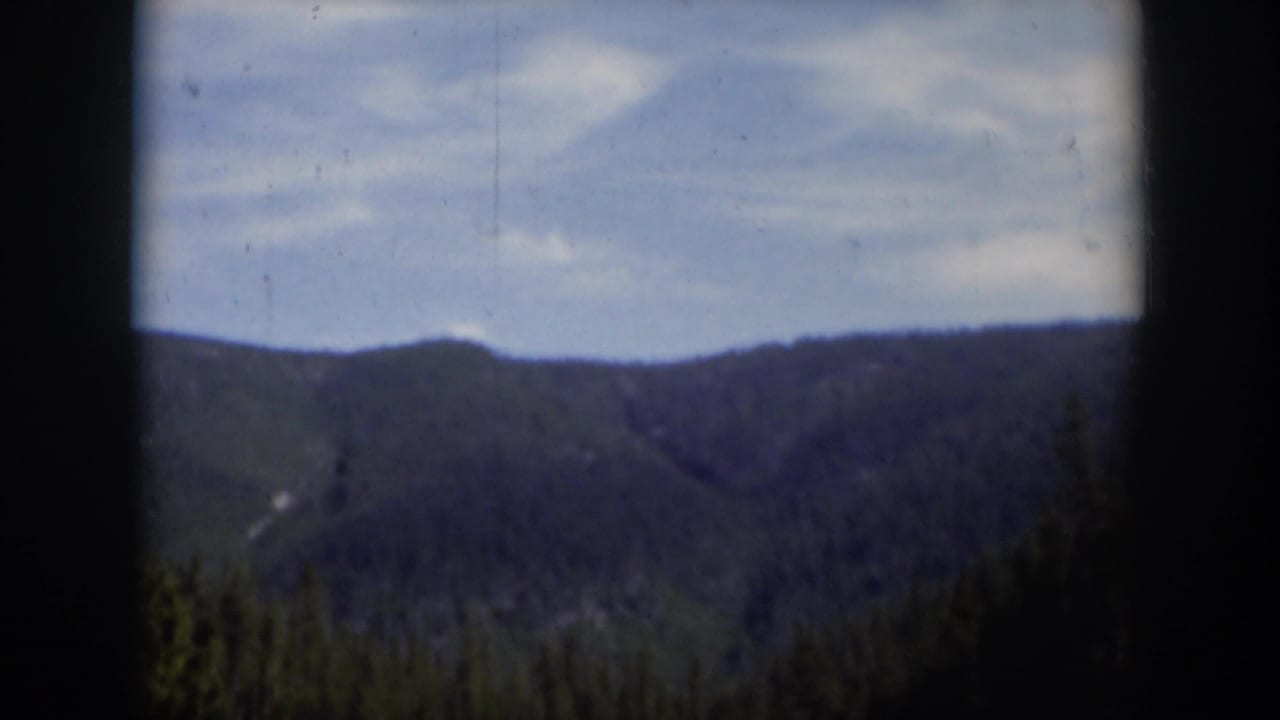 1951 Wyoming home-movie frame showing a hazy forested ridge, blue sky, and visible film wear along the image.
