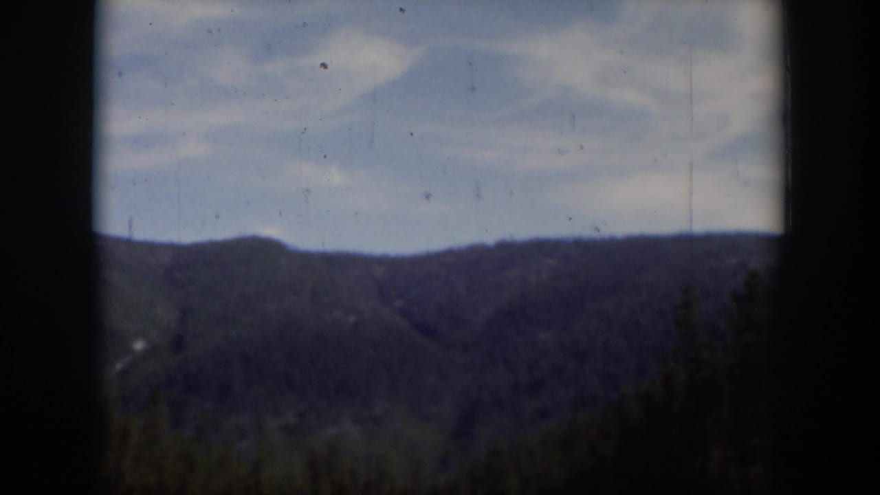 1951 Wyoming 8mm frame showing a distant wooded ridge, pale sky, and dark home-movie frame edges.