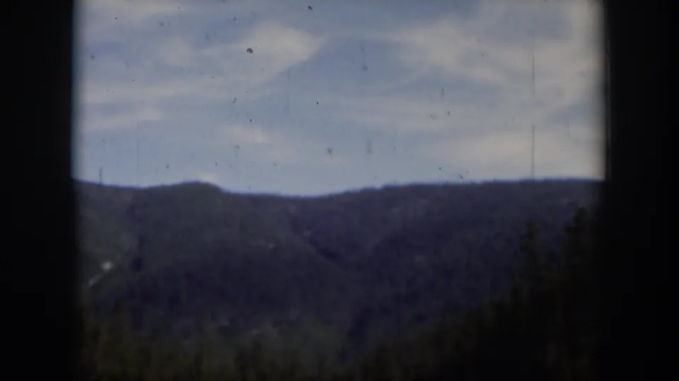 1951 Wyoming 8mm frame showing a distant wooded ridge, pale sky, and dark home-movie frame edges.