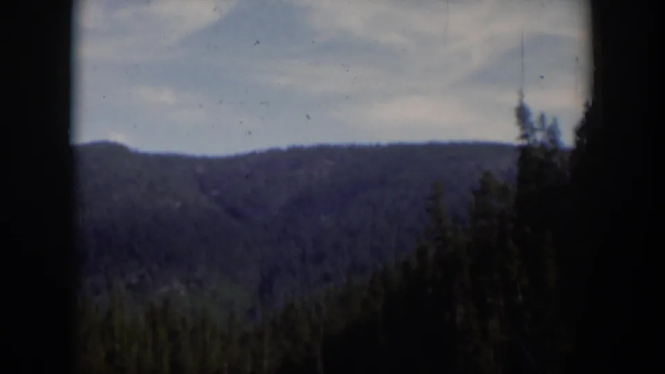 1951 Wyoming 8mm frame showing a distant forested mountain ridge under a pale sky with dark film borders.