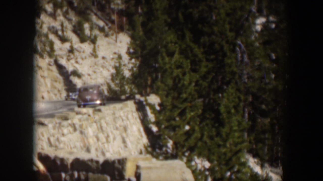 A classic car moves along a winding Wyoming mountain road in this 1951 8mm home-movie frame.