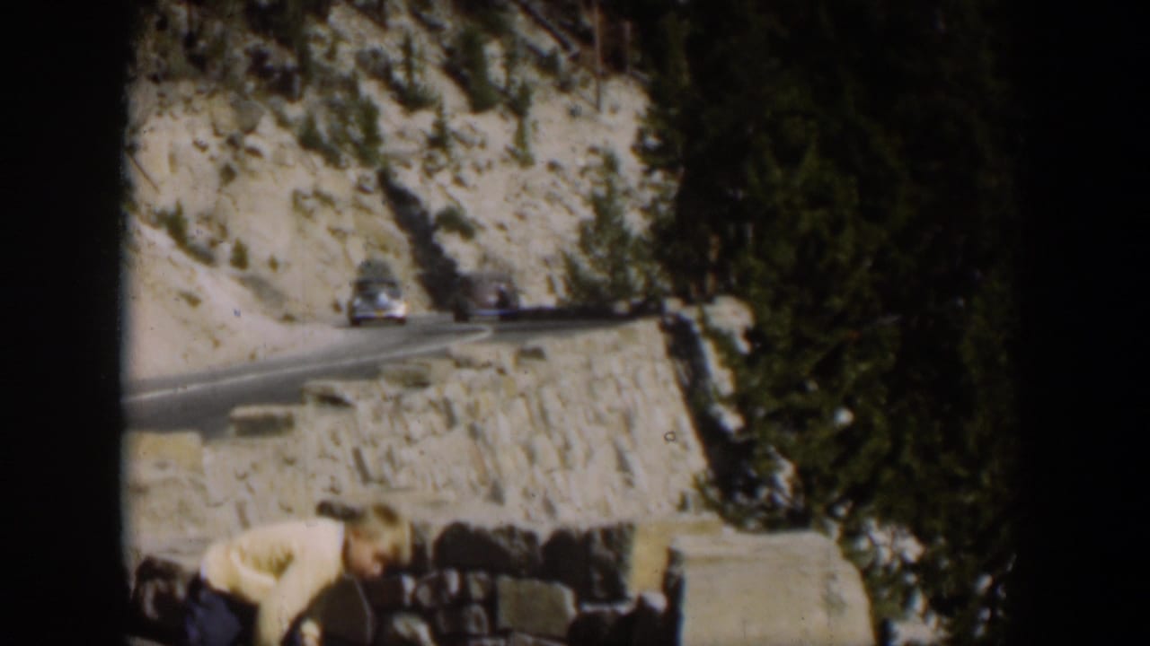 A boy bends in the foreground while cars move along a winding Wyoming mountain road in this 1951 home-movie frame.