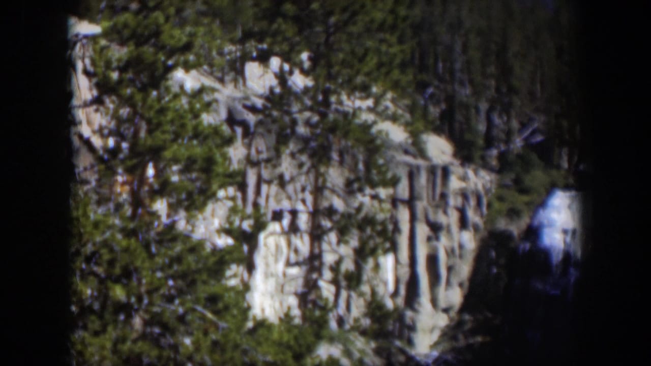 1951 Wyoming 8mm frame showing a bright waterfall near a rugged cliff, with pine branches and dark gate edges around the view.