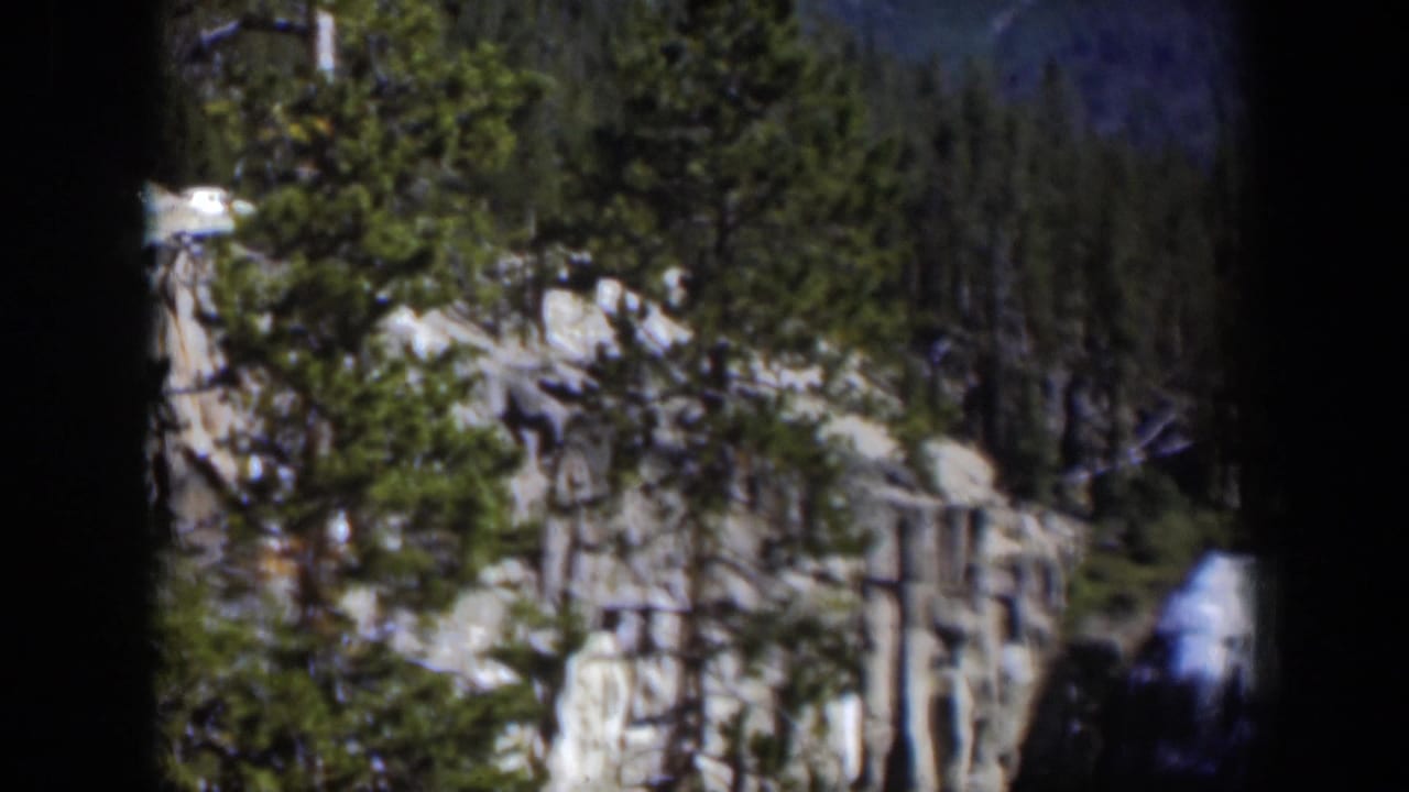 1951 Wyoming 8mm frame of a forested cliff landscape with a distant waterfall visible near the lower right edge.