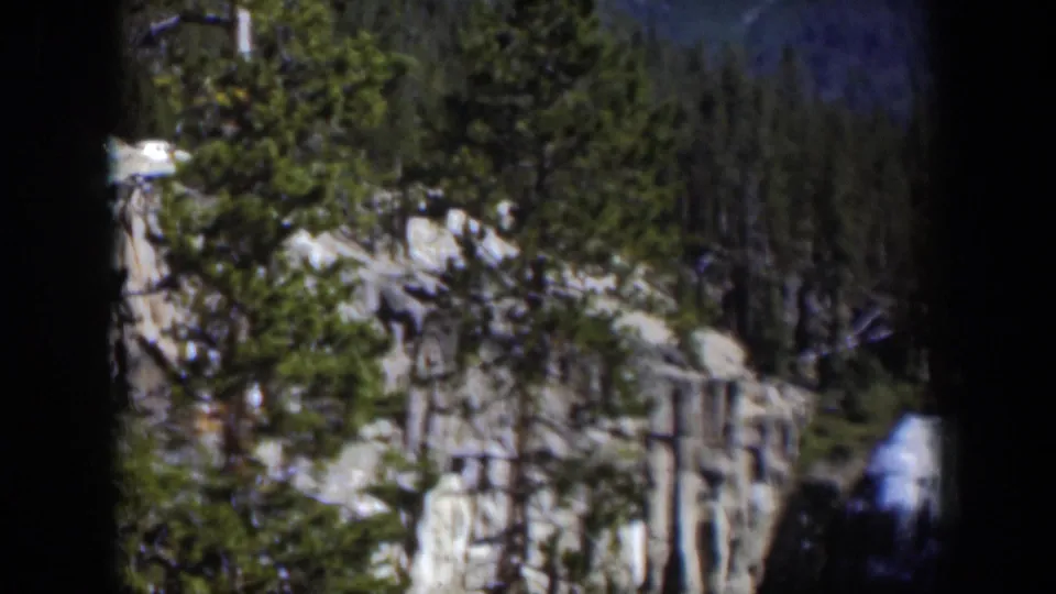 1951 Wyoming 8mm frame of a forested cliff landscape with a distant waterfall visible near the lower right edge.
