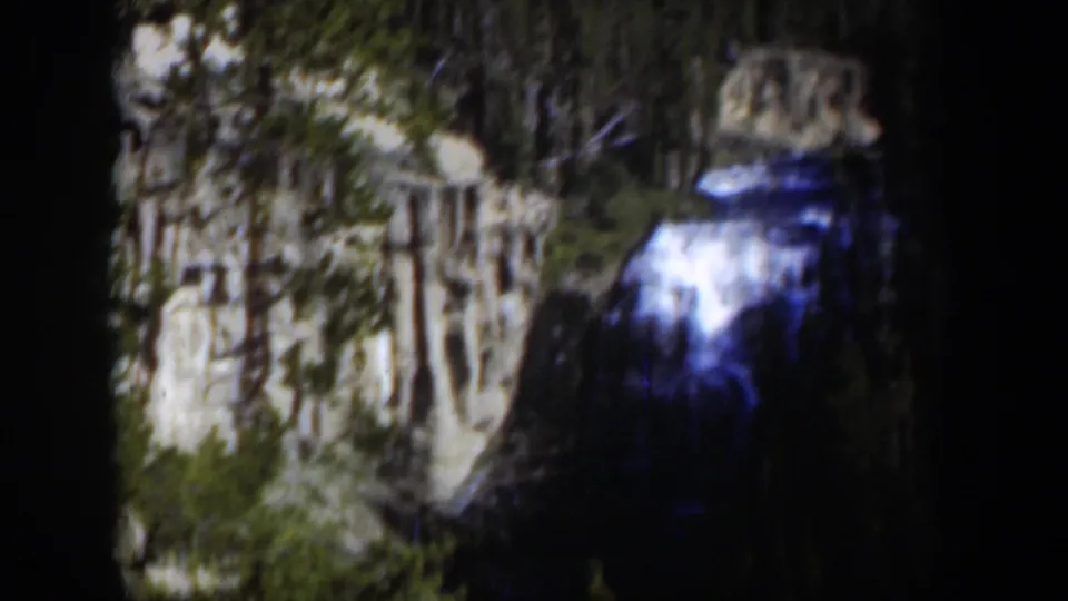 Vintage 8mm frame of a Wyoming waterfall near cliffs and trees, with heavy dark borders and soft low-light detail.