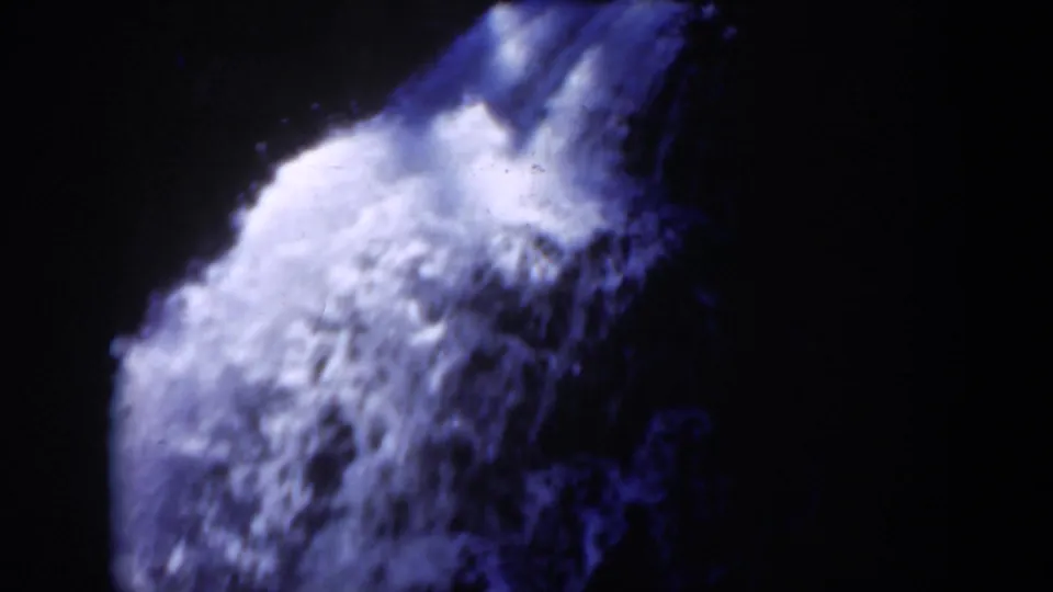 Close 1951 Wyoming home-movie view of rushing waterfall water, blue-lit against dark surrounding rock and forest shadow.