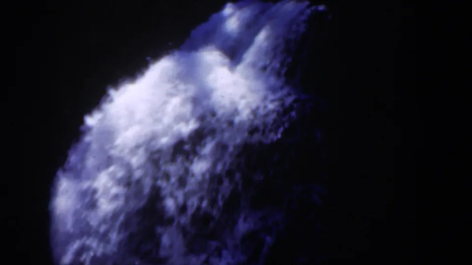 1951 Wyoming 8mm frame showing a bright rush of waterfall foam dropping over shadowed rock, with blue-purple film color and deep surrounding darkness.