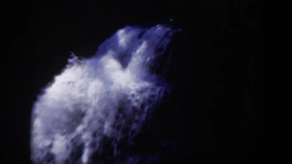 1951 Wyoming 8mm frame showing turbulent white water sliding and dropping across dark rock, with visible grain and a blue-tinted archival color shift.
