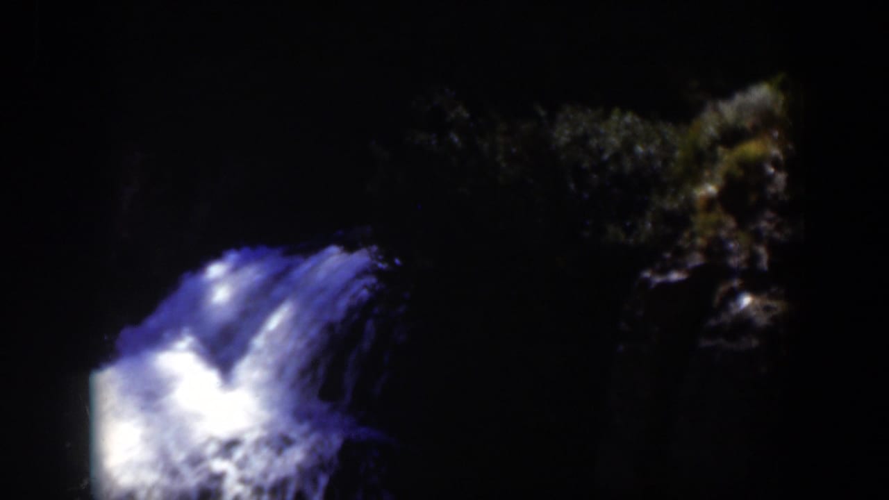1951 Wyoming 8mm frame showing the glowing cascade with a darker rocky bank and forest texture at the right.