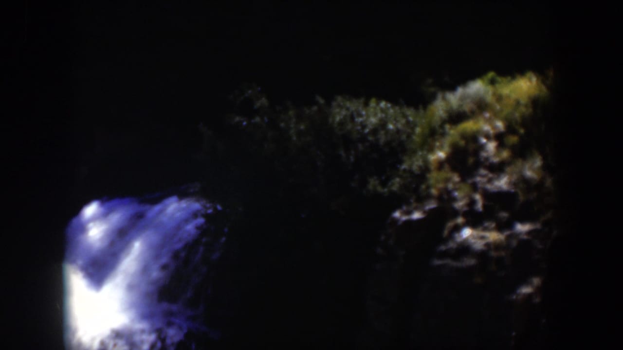 1951 Wyoming 8mm frame showing the waterfall lower in the frame, with shadowed forest and rock visible to the right.