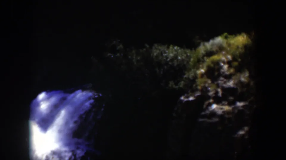 1951 Wyoming 8mm frame showing the waterfall lower in the frame, with shadowed forest and rock visible to the right.