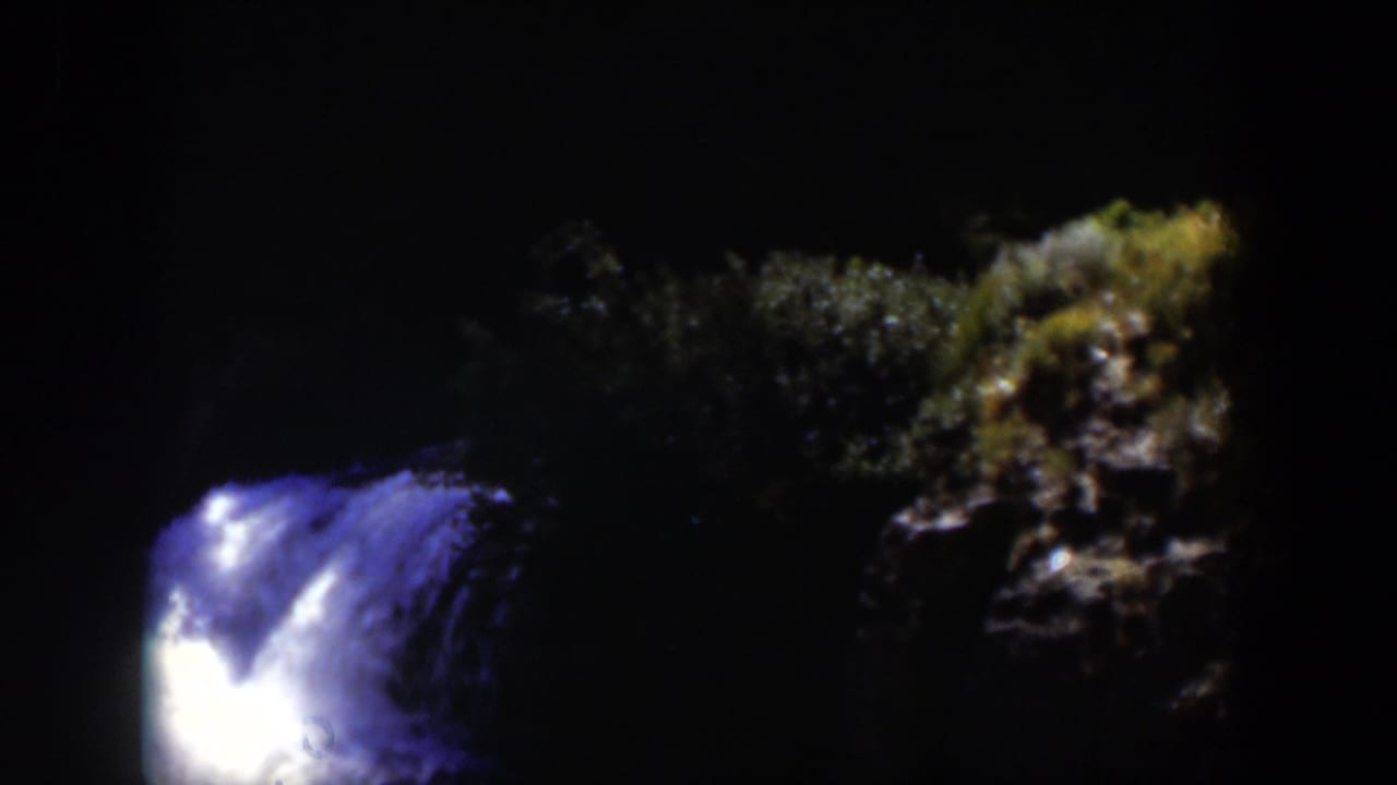1951 Wyoming-associated 8mm frame showing a bright blue-white water current against near-black rocks and faint foliage.