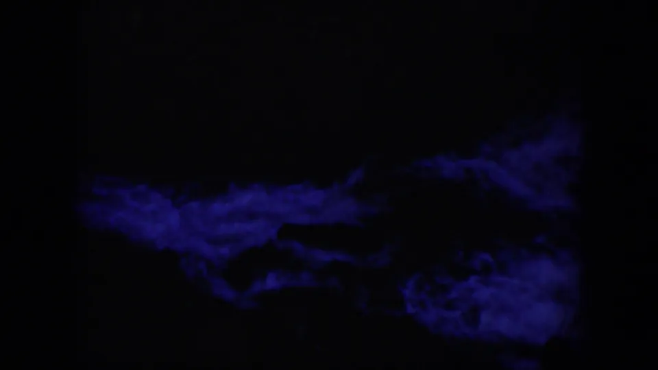 1951 Wyoming-associated 8mm frame with blue illuminated current moving below a large dark rock silhouette.