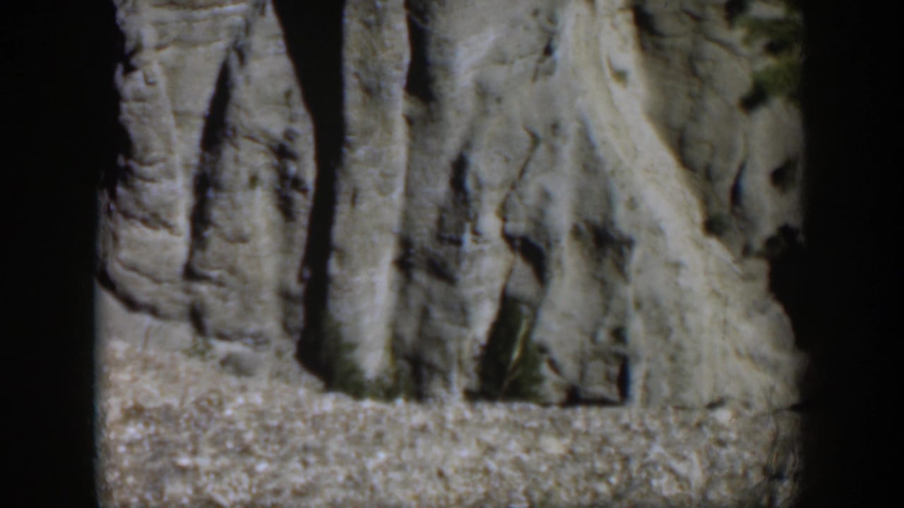 1951 Wyoming 8mm frame showing pale gray rock surfaces with vertical striations, rough ledges, and deep daylight shadows.