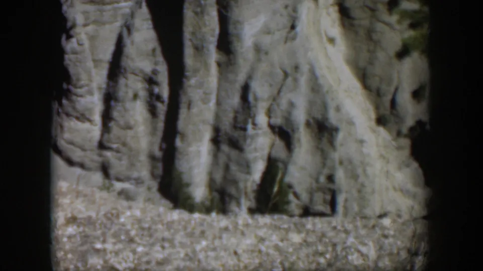 1951 Wyoming 8mm frame showing pale gray rock surfaces with vertical striations, rough ledges, and deep daylight shadows.