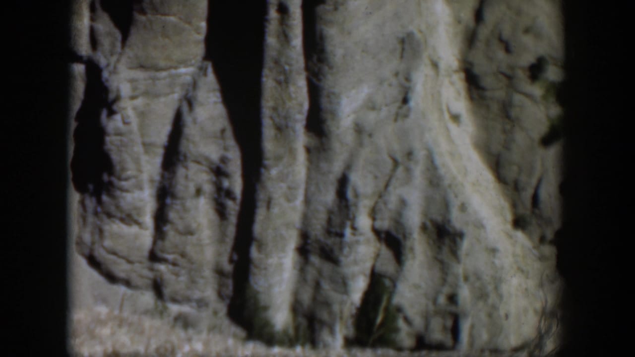 Close 8mm view of Wyoming rock formations, with pale stone, narrow crevices, and soft mid-century film grain.