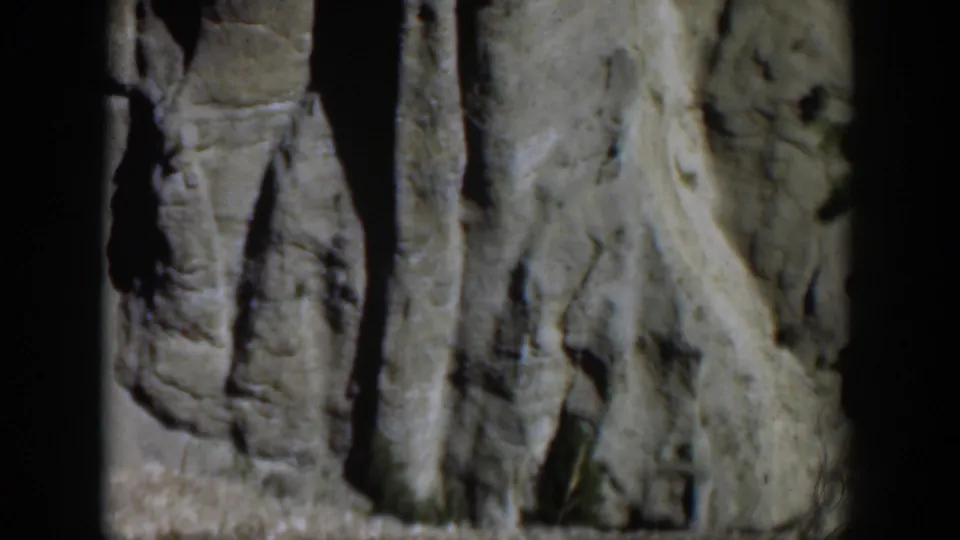Close 8mm view of Wyoming rock formations, with pale stone, narrow crevices, and soft mid-century film grain.
