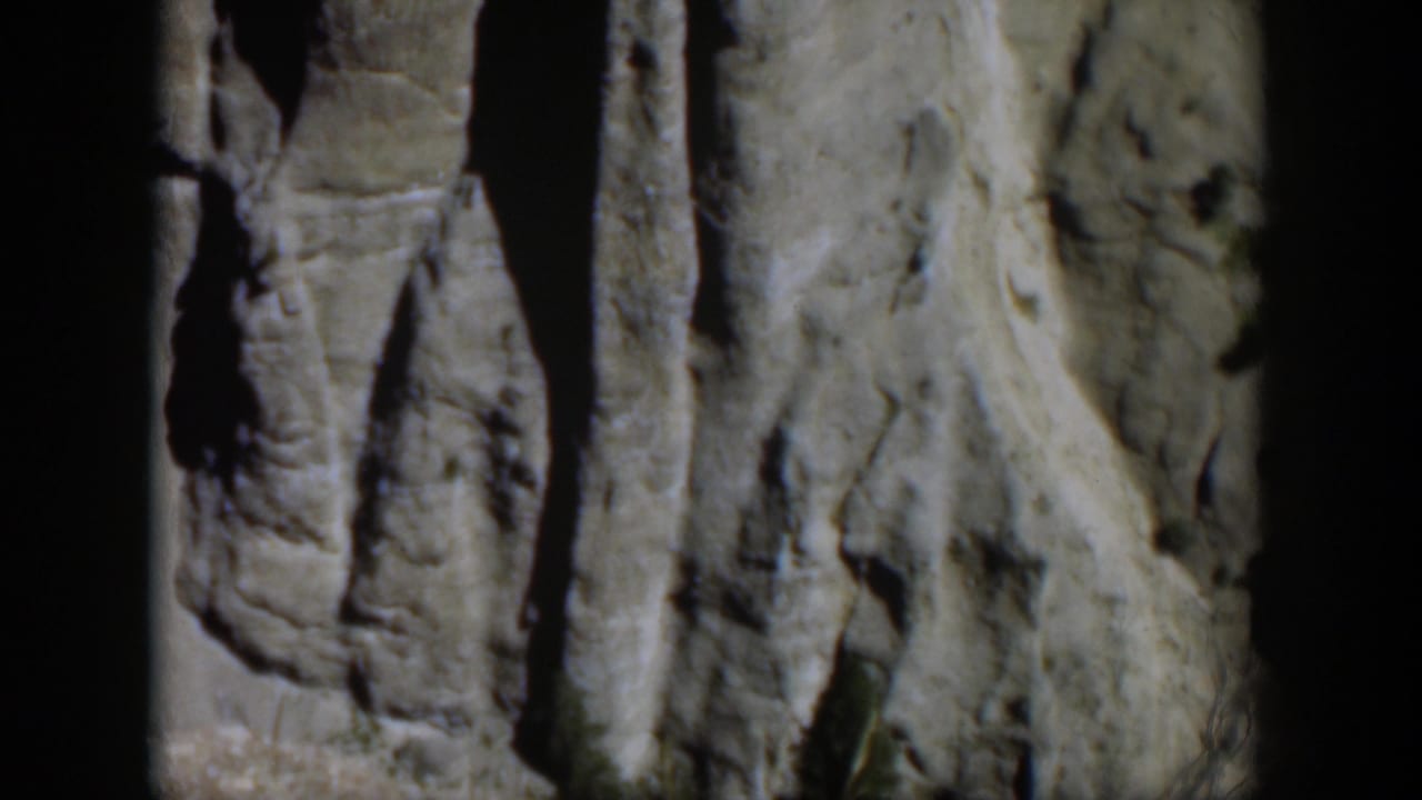1951 Wyoming home-movie frame showing gray rock columns beside a sloped pale stone face under bright sun.