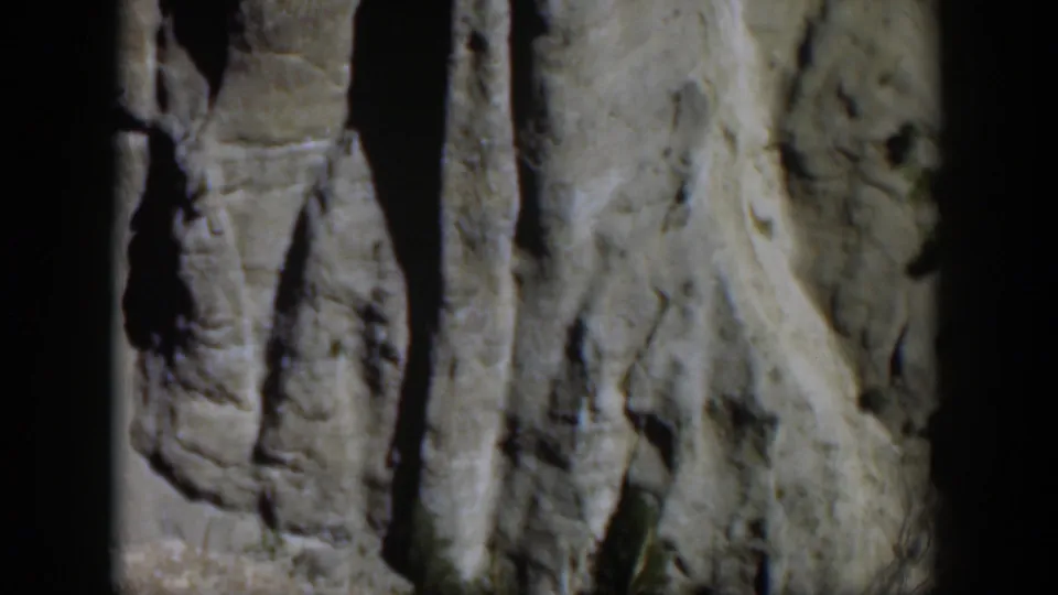 1951 Wyoming home-movie frame showing gray rock columns beside a sloped pale stone face under bright sun.