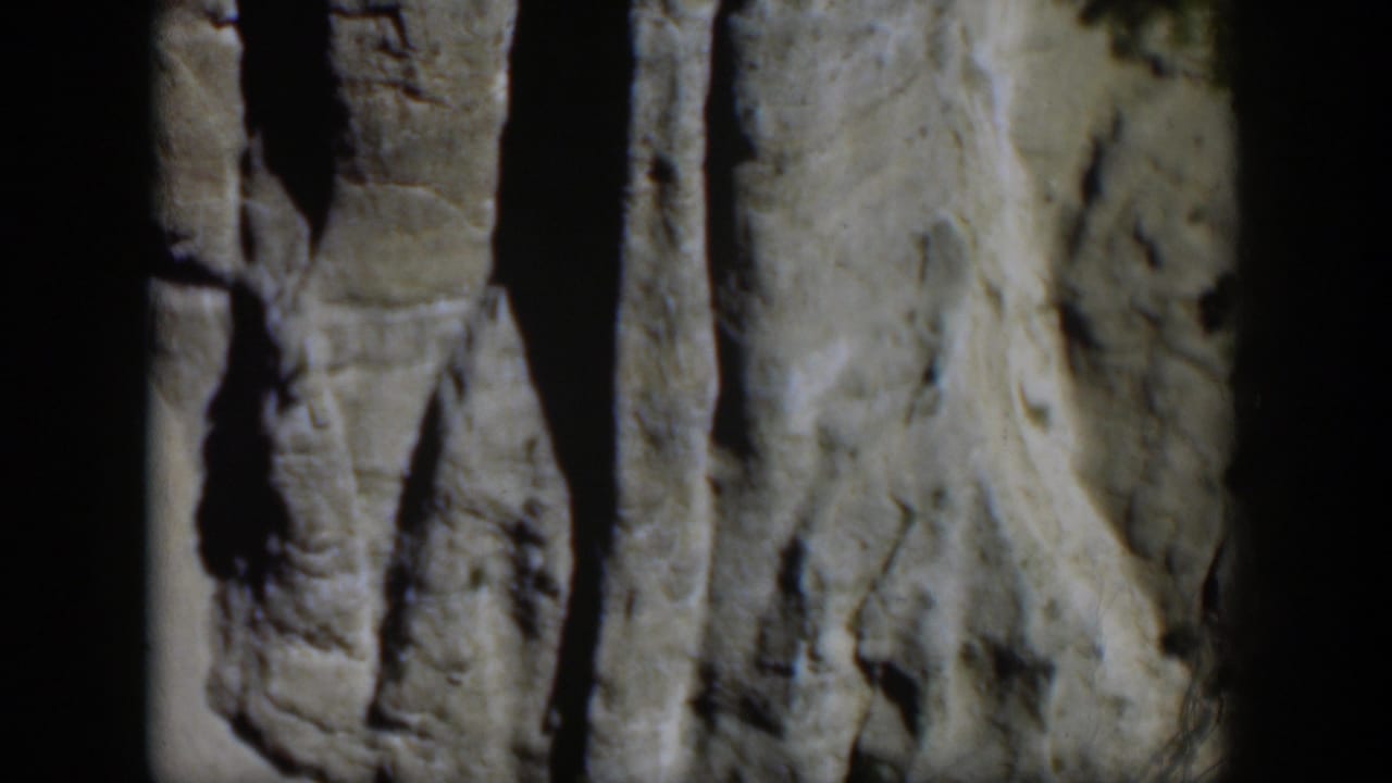 Wyoming 1951 8mm frame of weathered gray rock, dark vertical shadow lines, and pale textured stone in daylight.
