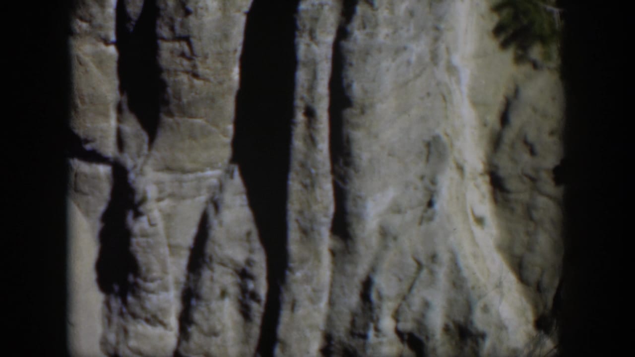 Steep pale canyon wall with dark shadows beside a partial overhead view of river water.