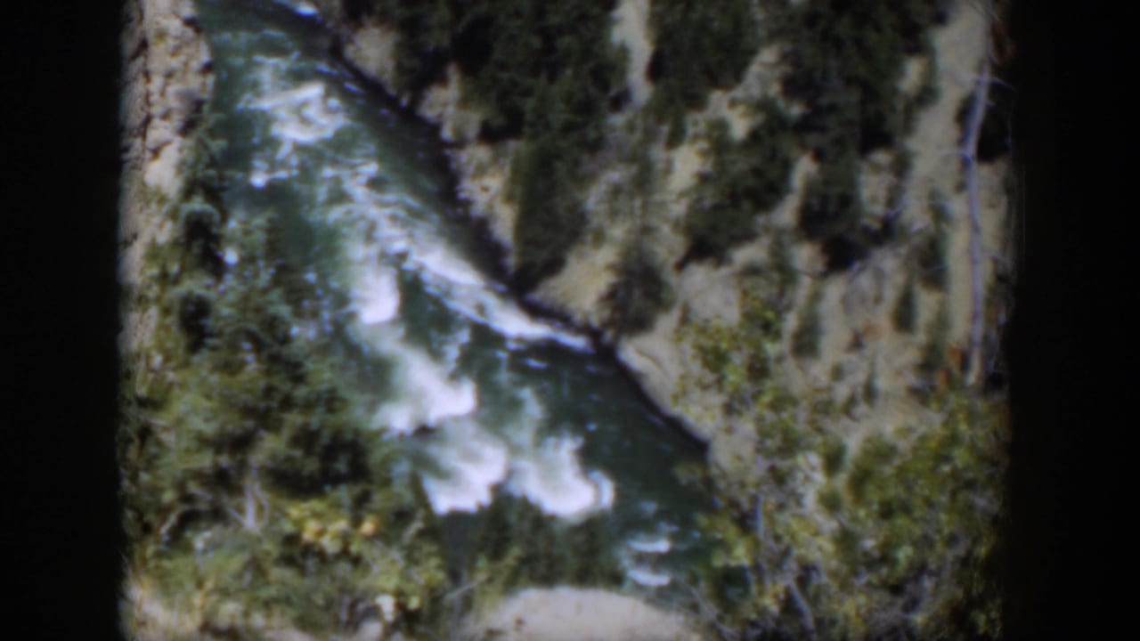 1951 Wyoming 8mm frame showing river rapids cutting through a rocky canyon with dense trees on the slopes.