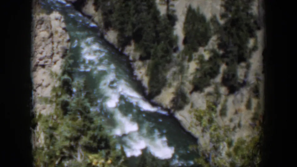 1951 Wyoming 8mm frame of a white-water river below pale canyon rock and evergreen vegetation.