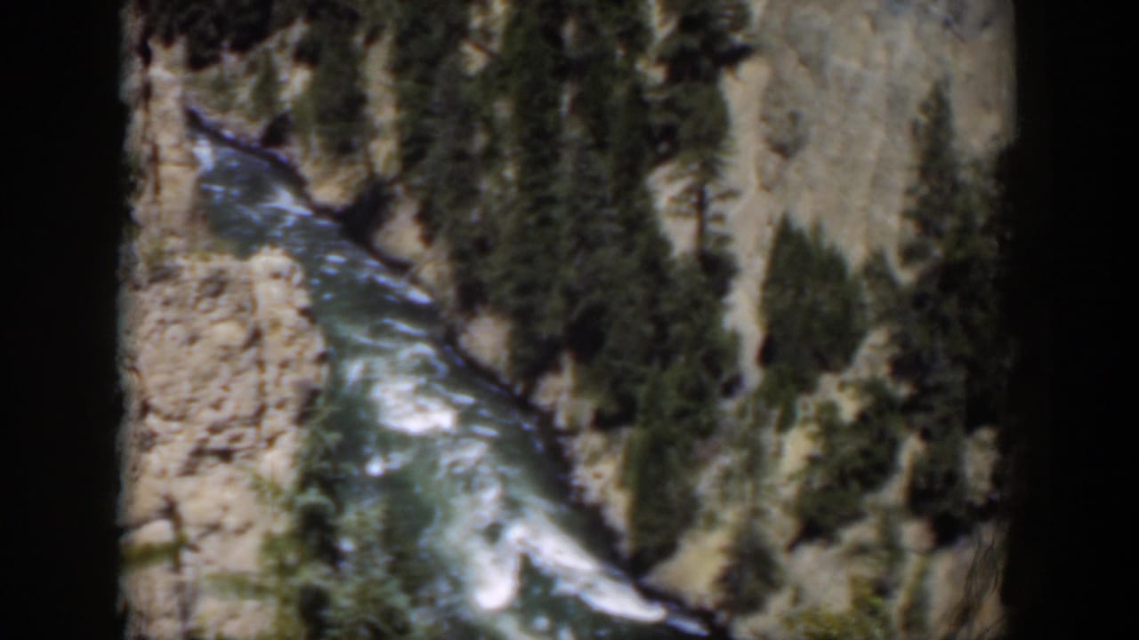 1951 Wyoming 8mm frame looking down on a river channel, white rapids, pale cliffs, and scattered evergreens.