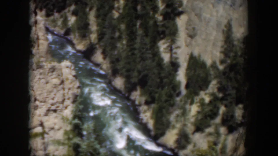 1951 Wyoming 8mm frame looking down on a river channel, white rapids, pale cliffs, and scattered evergreens.