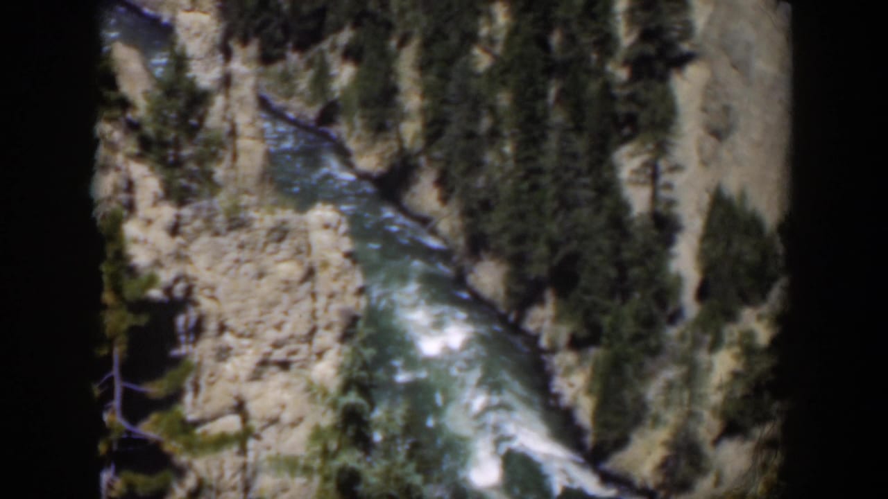 1951 Wyoming 8mm view of a rushing mountain river framed by canyon rock, evergreens, and rounded film borders.