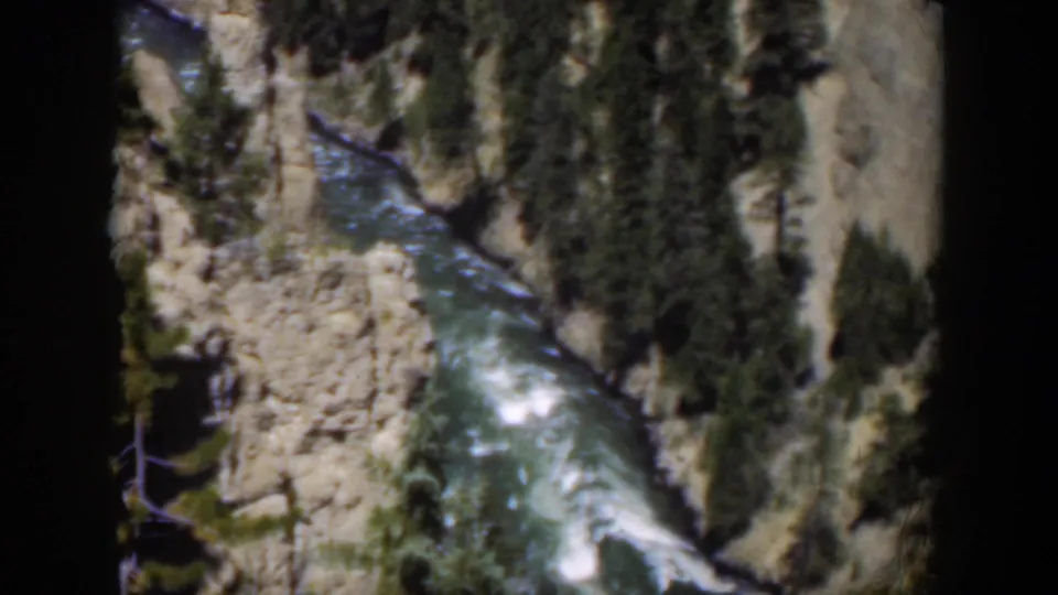 1951 Wyoming 8mm view of a rushing mountain river framed by canyon rock, evergreens, and rounded film borders.