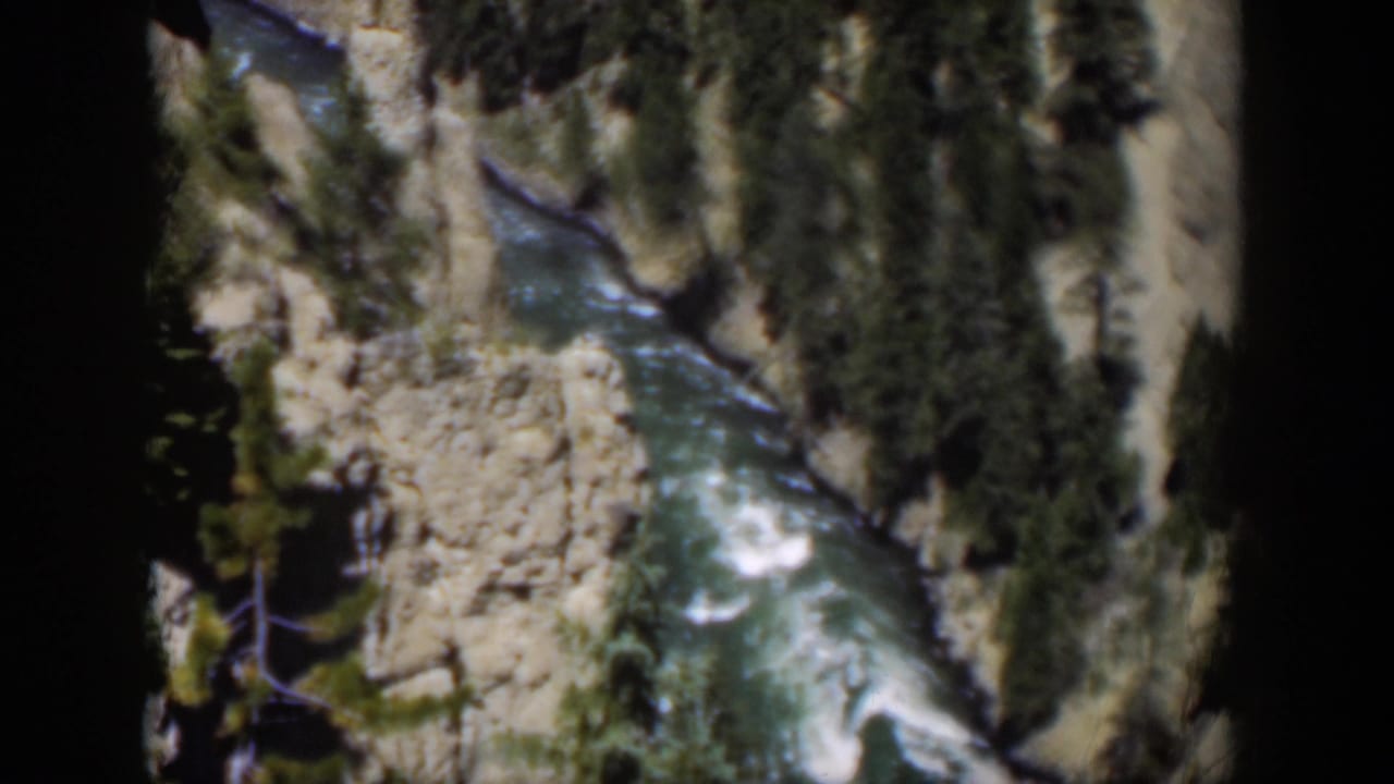 Winding river below rocky canyon slopes with evergreen trees and dark film borders.