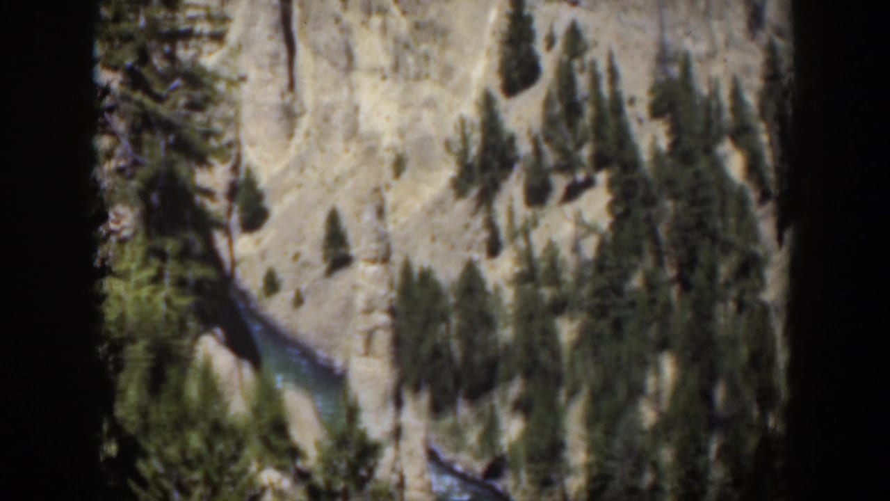 1951 Wyoming home-movie frame showing canyon rock, scattered evergreens, and a river descending through the scene.