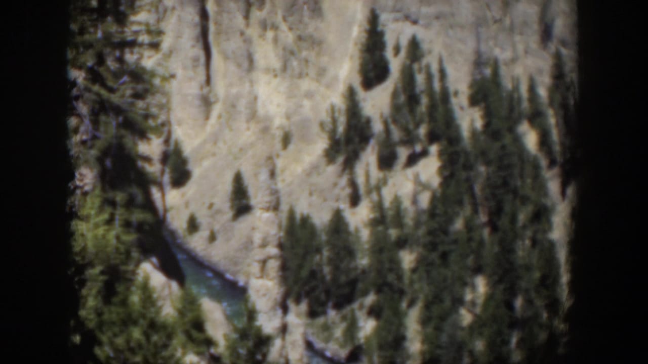 1951 Wyoming 8mm frame showing a turquoise river bend below pale canyon walls and scattered pine trees.