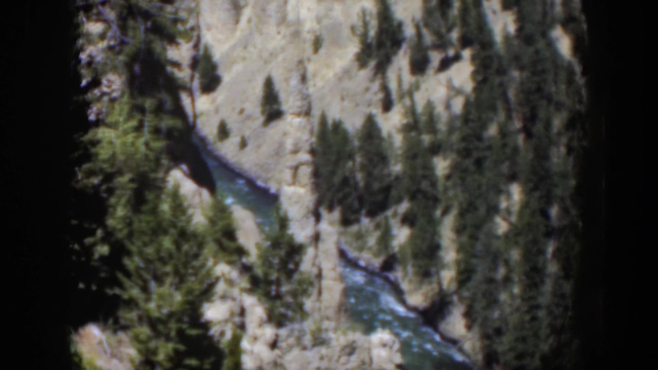 1951 Wyoming 8mm frame showing blue-green water and rapids below a rocky canyon slope with pines.