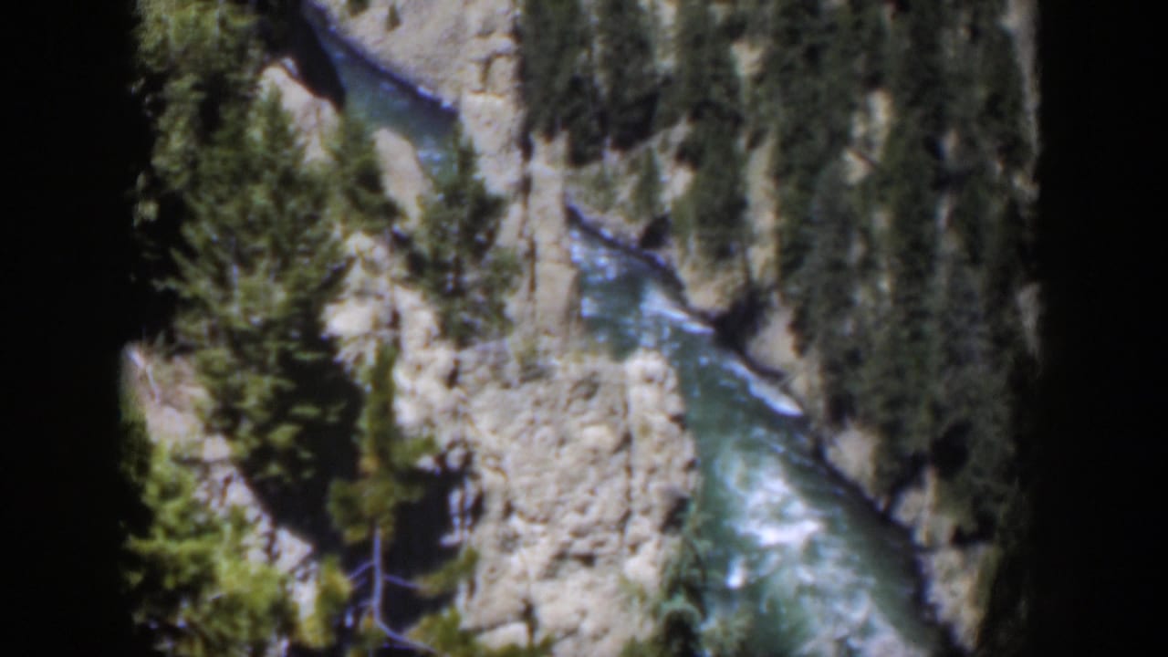 1951 Wyoming 8mm frame showing a river bend with white rapids below steep canyon banks and scattered pine trees.