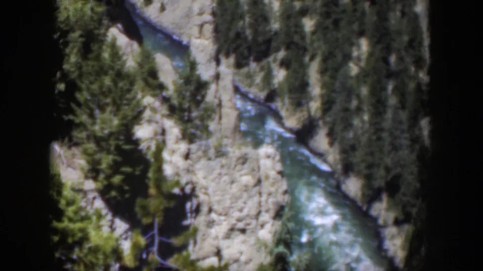 1951 Wyoming 8mm frame showing a river bend with white rapids below steep canyon banks and scattered pine trees.