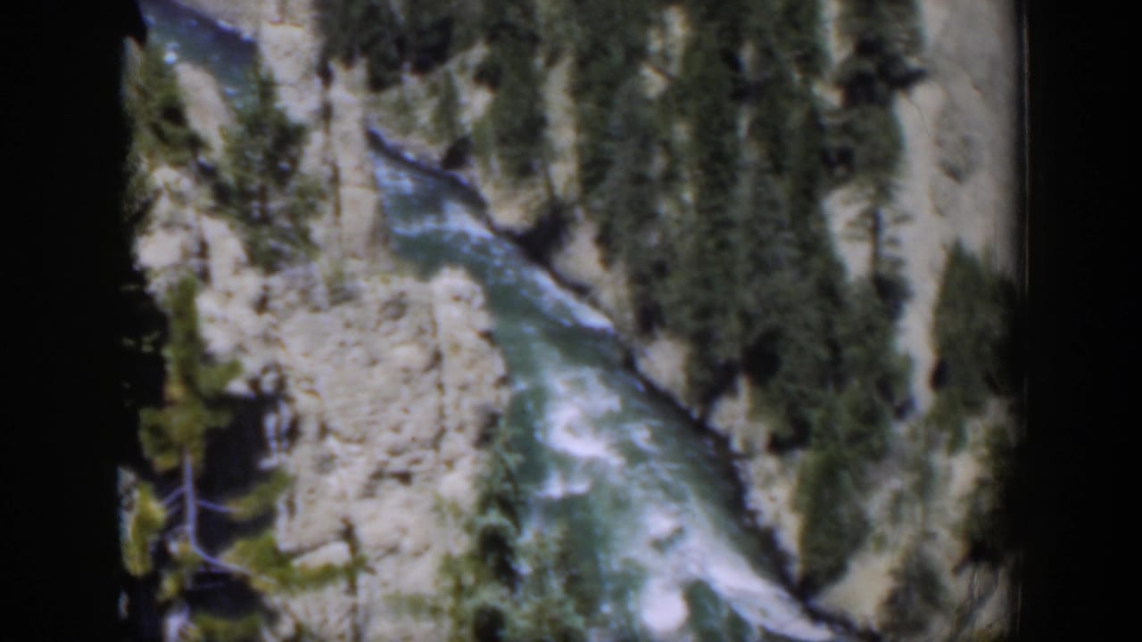 1951 Wyoming 8mm still of whitewater rapids below an elevated viewpoint, framed by canyon rock and conifers.