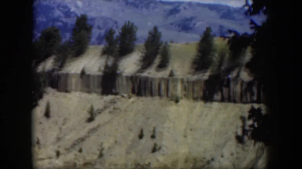 1951 Wyoming 8mm frame showing a pale ridge, vertical cliff texture, scattered pines, and blue mountain ridges from above.